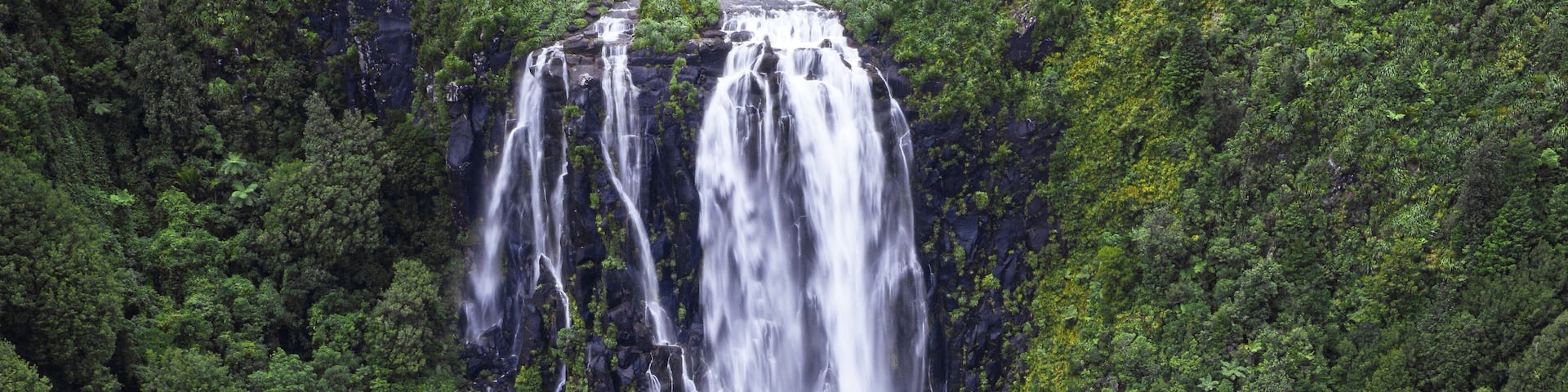 A multi-tiered waterfall cascading through a dense, green forest.
