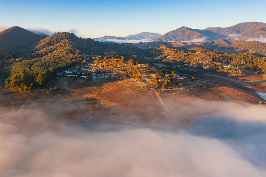 Aerial view of a caravan park on the shores of a mountain lake covered in fog