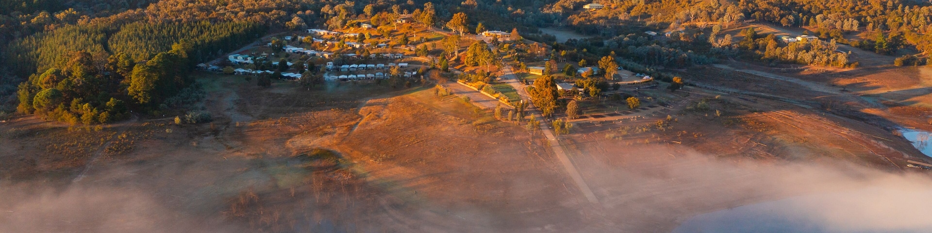 Aerial view of a caravan park on the shores of a mountain lake covered in fog