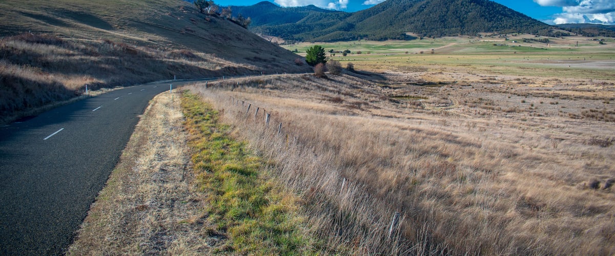 A winding road through a hilly landscape with a clear sky and distant mountains.