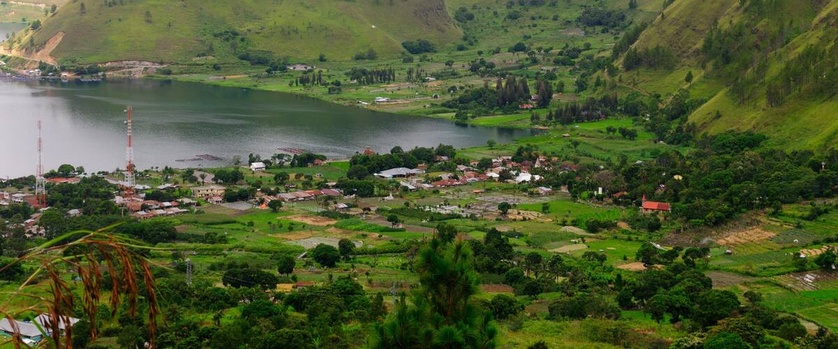A valley with a lake, green hills, and a small town with buildings and houses.