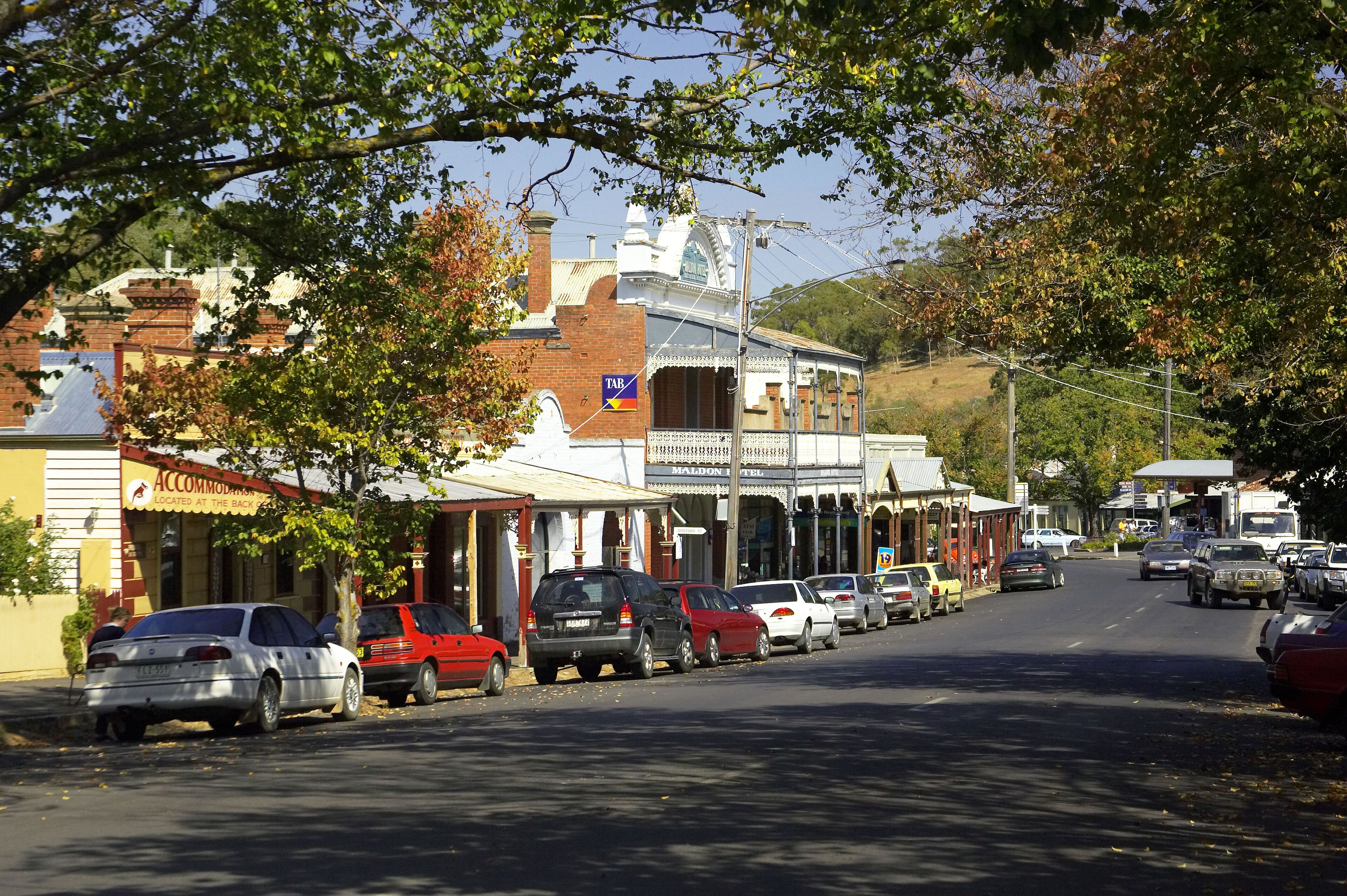 A street lined with vintage buildings, parked cars, and trees.