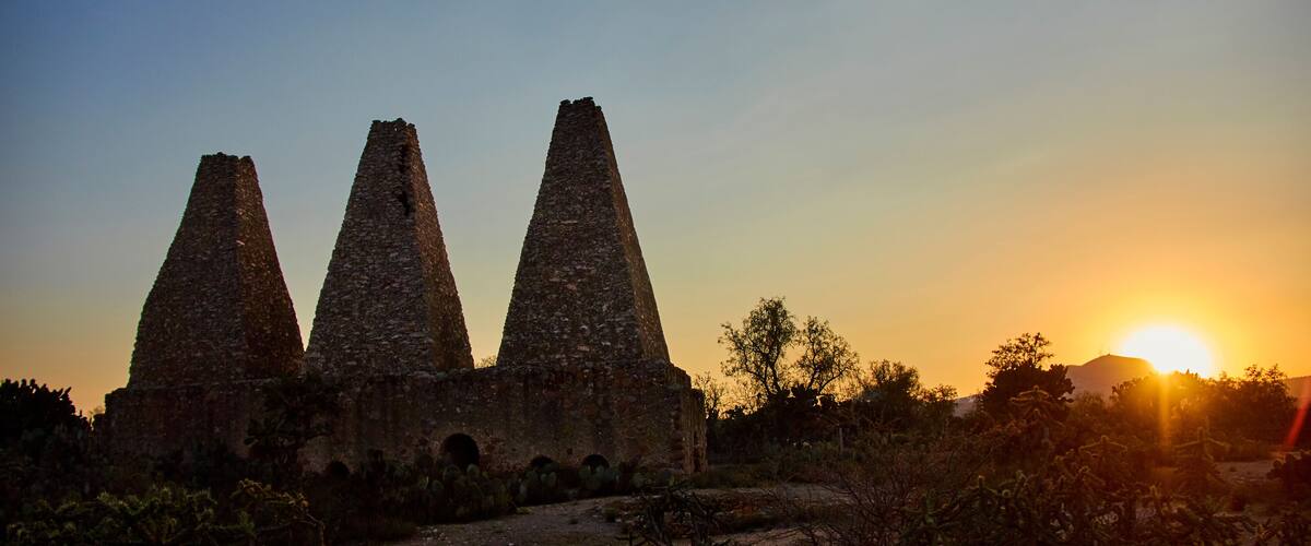 Three stone pyramids at sunset with the sun setting behind them.