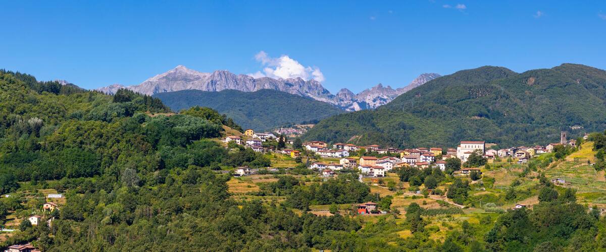 A mountainous landscape with a village nestled among green hills and a prominent mountain range in the background.
