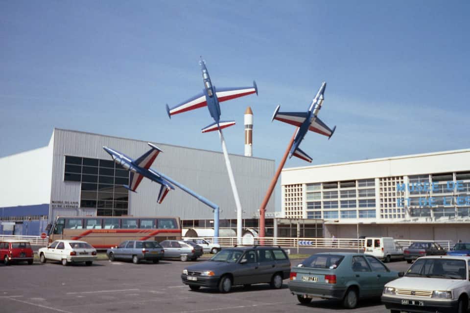 A parking lot with several cars and a building with a large window and a sign.