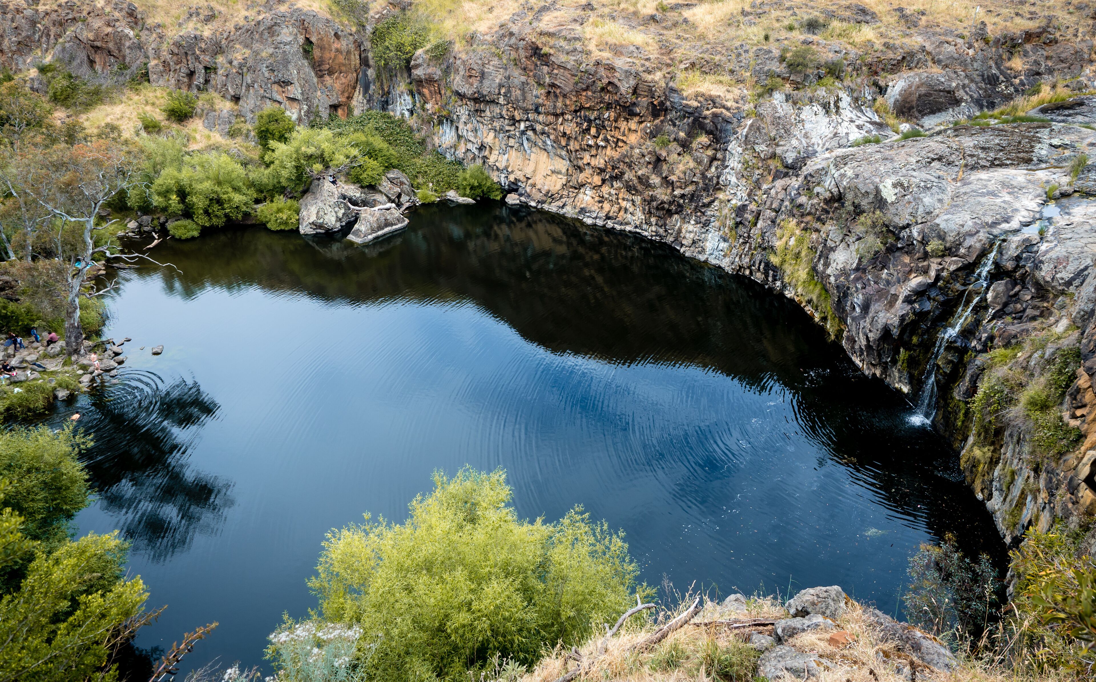 A natural pool surrounded by rocky cliffs and sparse vegetation.