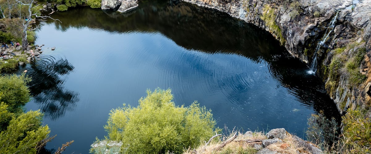 A natural pool surrounded by rocky cliffs and sparse vegetation.