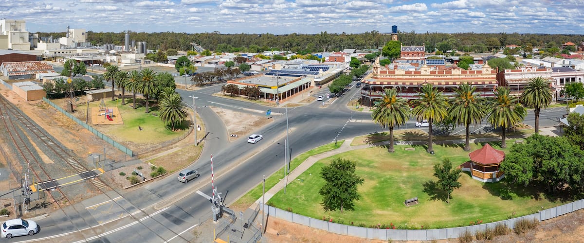 A town with a railway crossing, palm trees, and a prominent building with a clock tower.