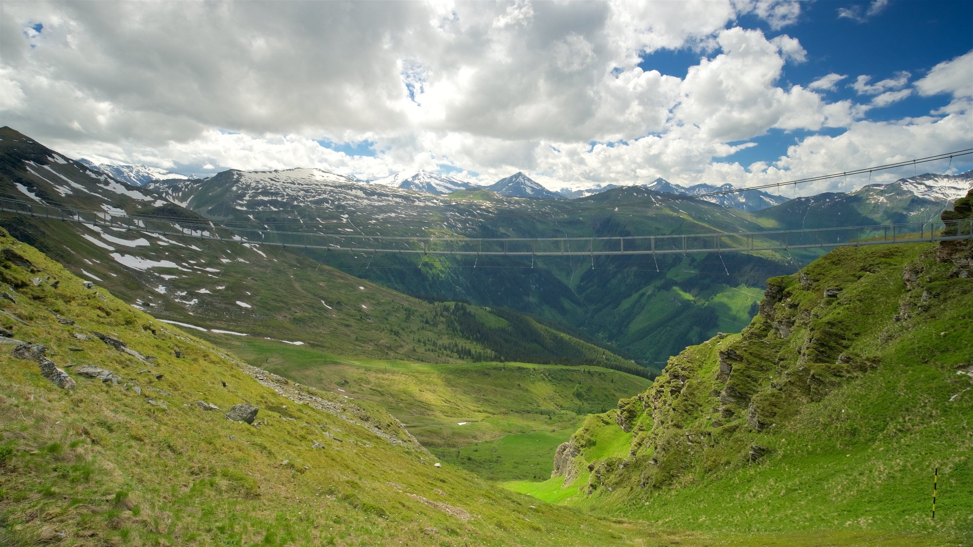 A mountain landscape with a suspension bridge and snow-capped peaks.