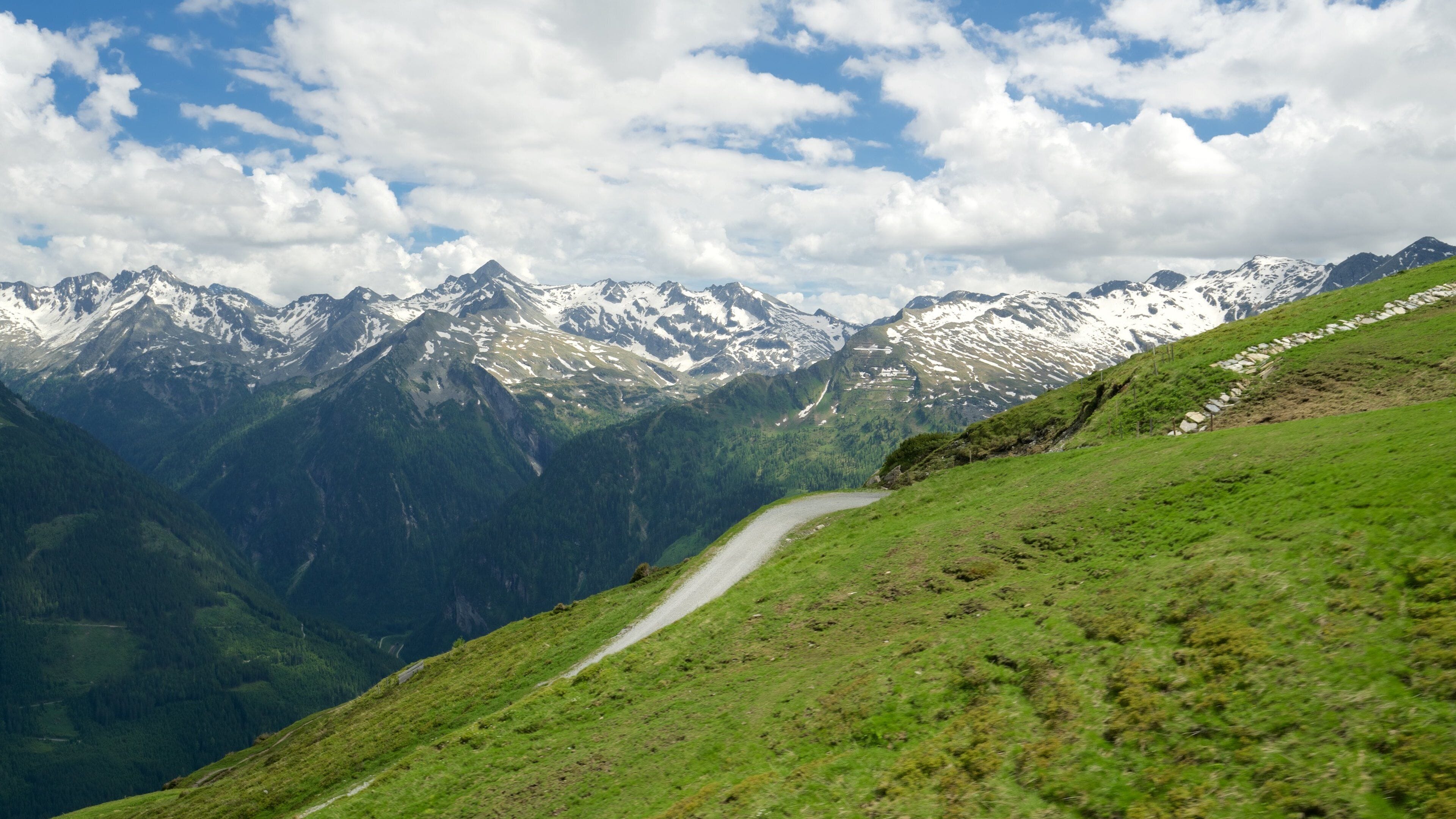 A winding mountain road with snow-capped peaks in the background.