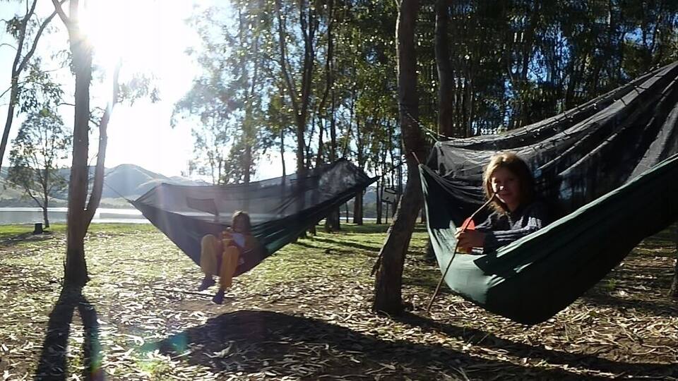 A hammock between trees, a covered vehicle, and a lake in the background.