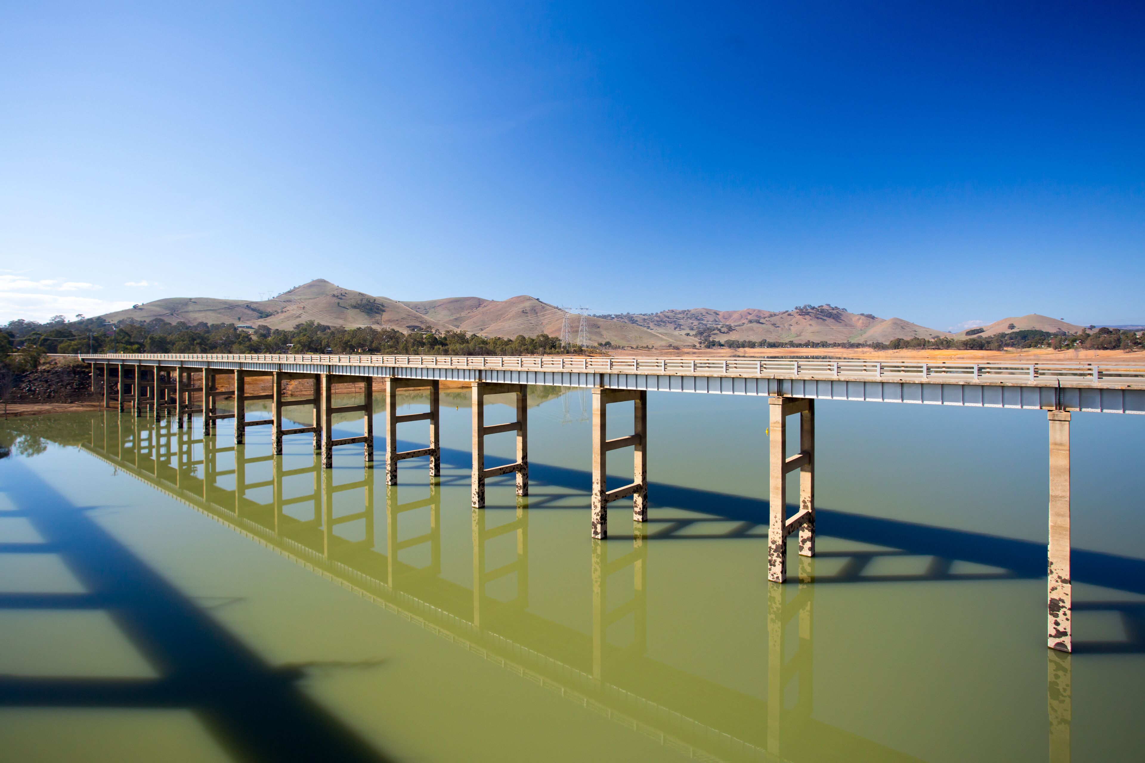 A bridge over a calm body of water with mountains in the background.