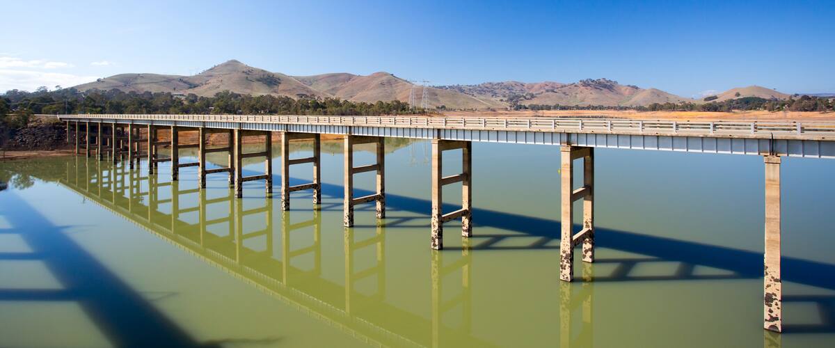 A bridge over a calm body of water with mountains in the background.