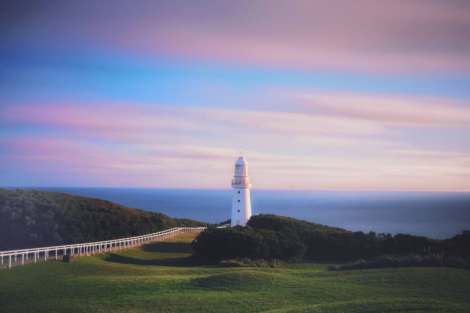 Un faro bianco su una collina erbosa, con un recinto bianco che conduce ad esso.
