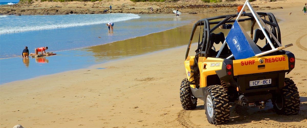 A beach with a yellow surf rescue vehicle parked on the sand.