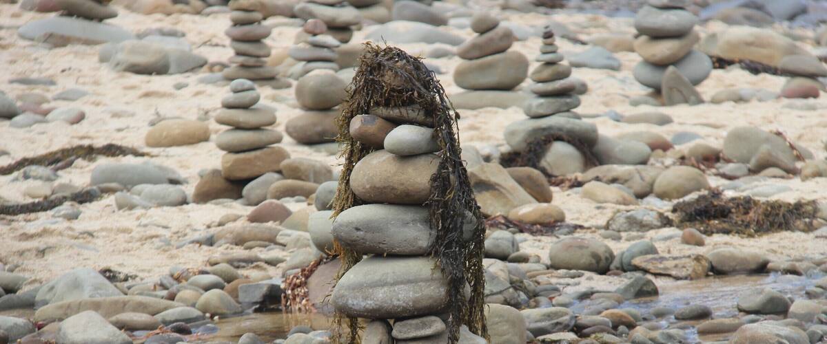 A stack of smooth, rounded stones balanced on a sandy beach with a stream flowing through.