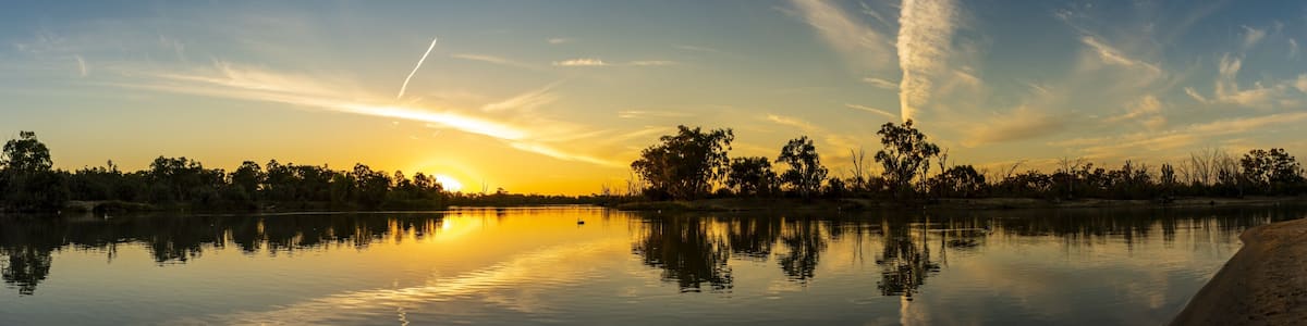 A sunset over a calm lake with reflections, trees, and a clear sky.