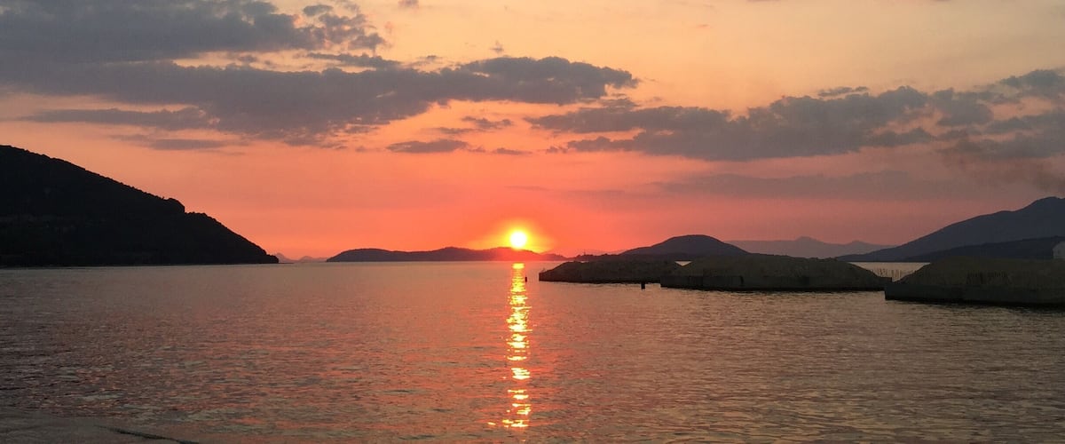 Un atardecer sobre una superficie acuática tranquila con una costa lejana y algunas islas pequeñas.
