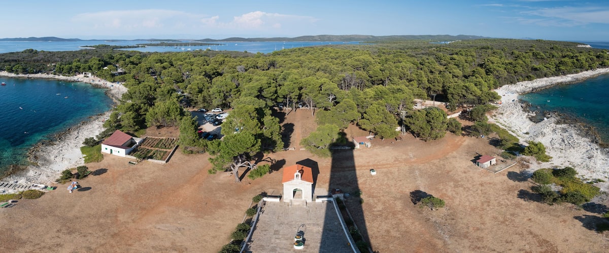 An aerial view of a coastal area with a small church, a sandy beach, and a forested island.