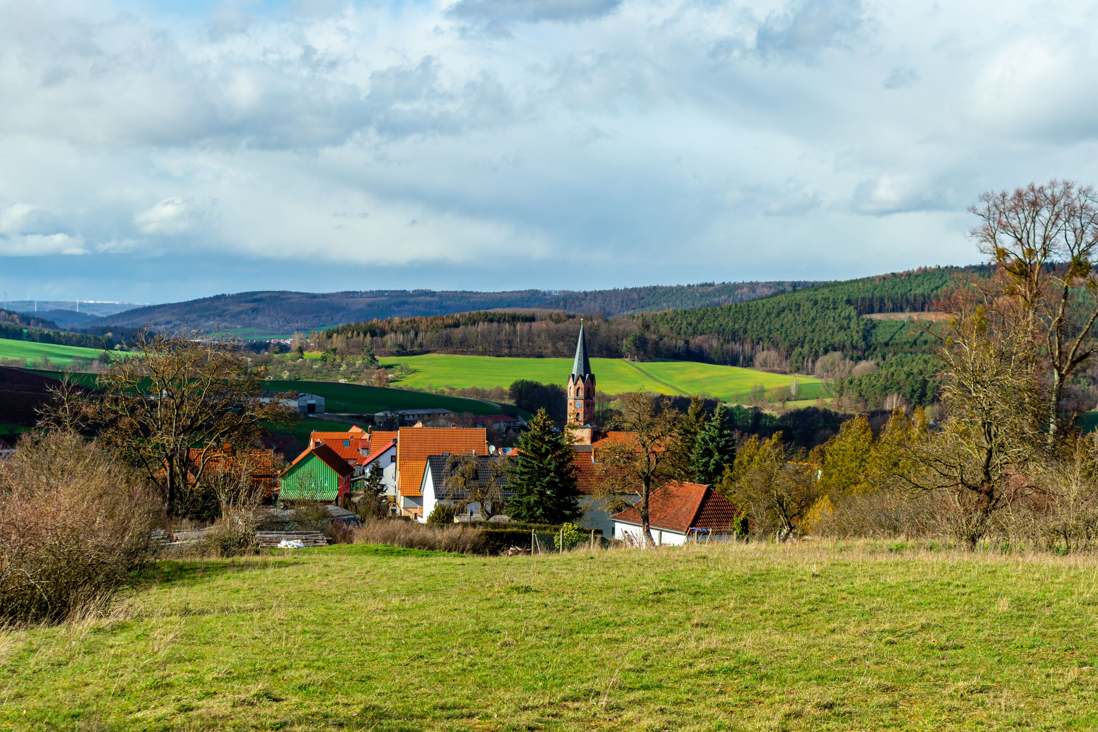 A village with a church, green fields, and rolling hills in the background.