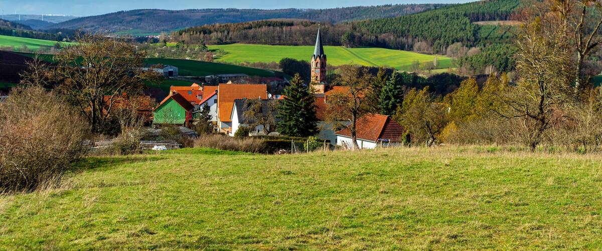 A village with a church, green fields, and rolling hills in the background.