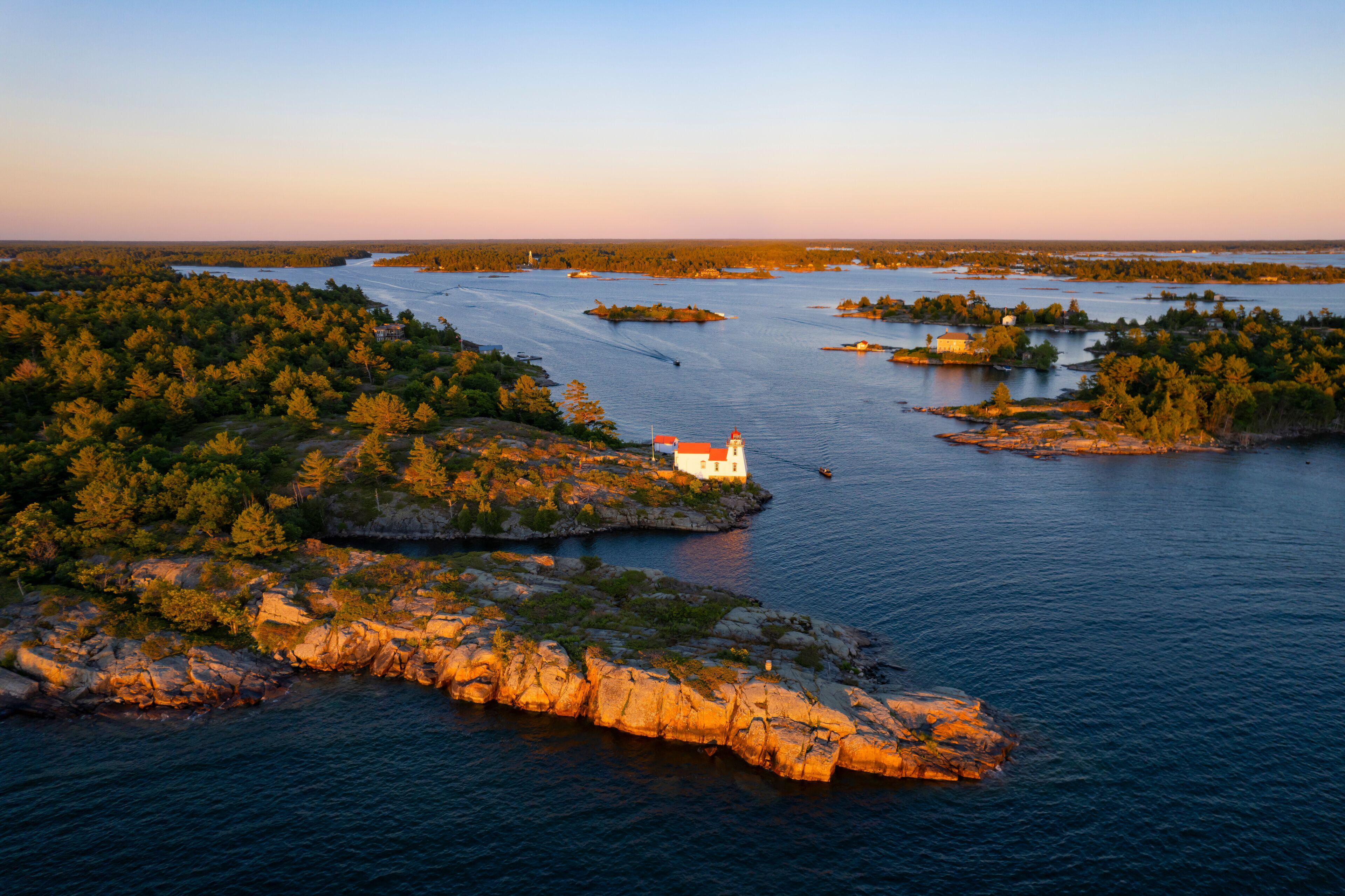 Aerial view of Pointe au Baril Lighthouse, islands, and forest with rocky shoreline at sunset, Georgian Bay, Canada.