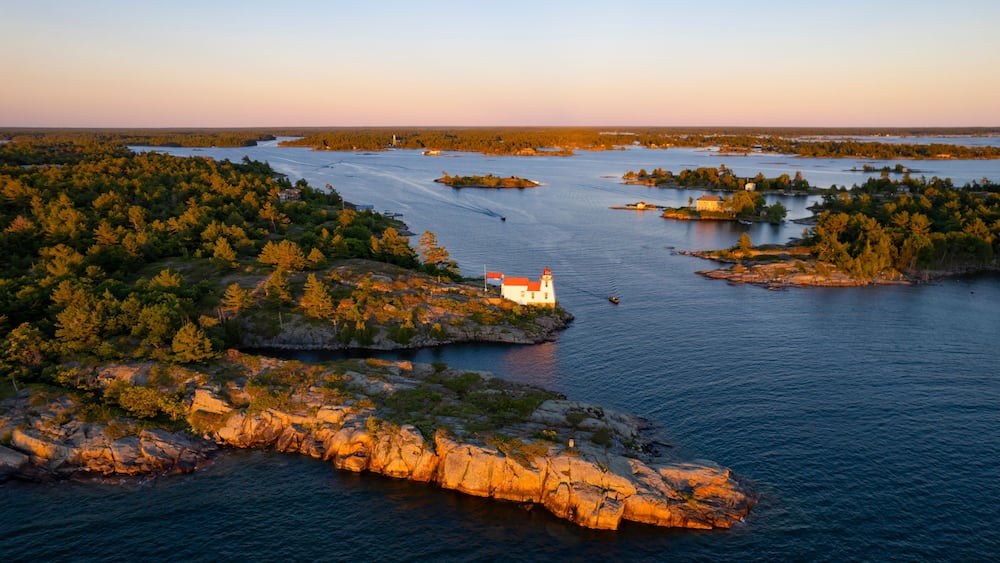Un paysage côtier avec un phare perché sur un promontoire rocheux, entouré de forêts denses et bordé d’une baie paisible.
