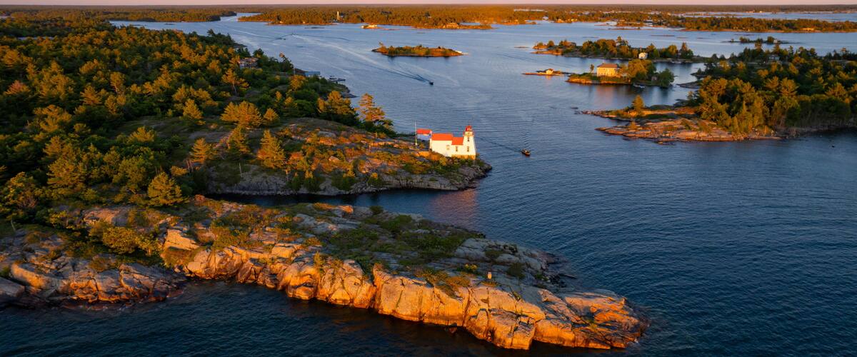 A coastal landscape with a lighthouse on a rocky outcrop, surrounded by dense forests and a calm bay.