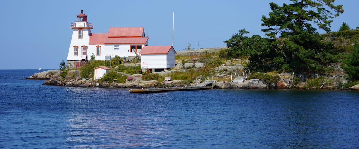 A lighthouse on a rocky island with a red roof, surrounded by water and greenery.