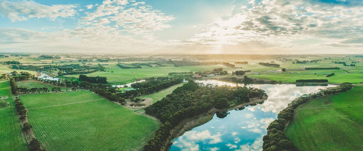 A river meandering through green fields, surrounded by trees and small buildings.