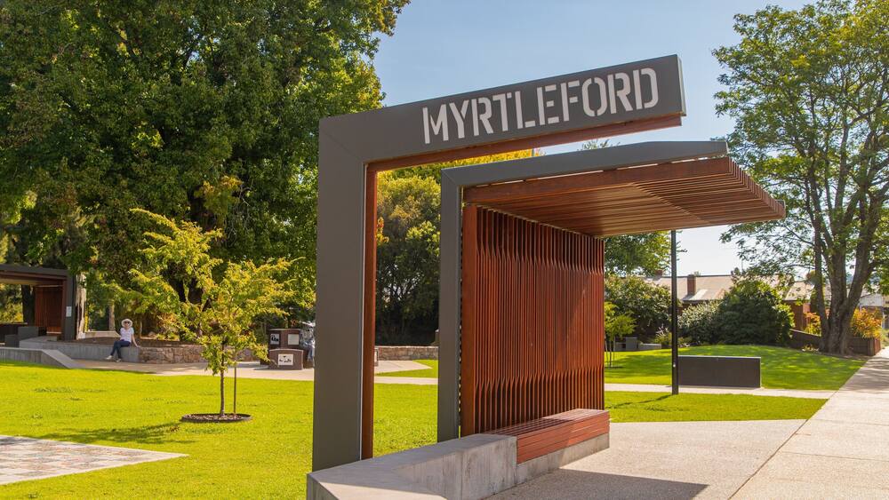 Un panneau indiquant « MYRTLEFORD », avec une structure moderne et une zone verdoyante parsemée d’arbres.