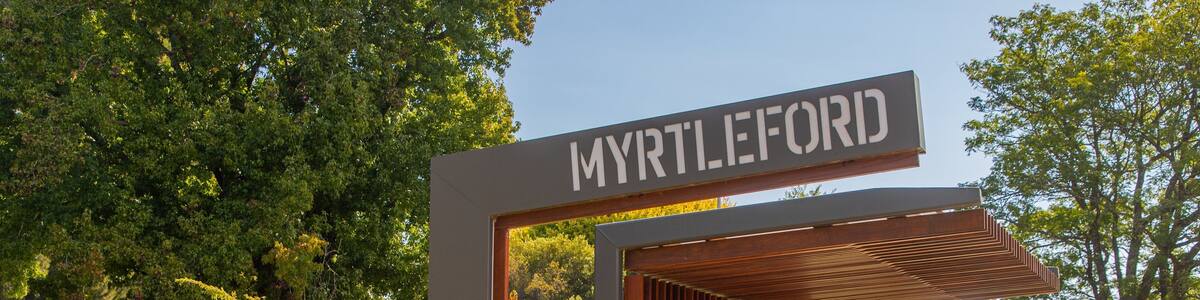 Un panneau indiquant « MYRTLEFORD », avec une structure moderne et une zone verdoyante parsemée d’arbres.