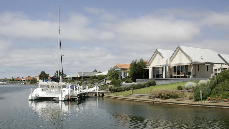 A marina with boats docked, a house with a white roof, and a calm river.