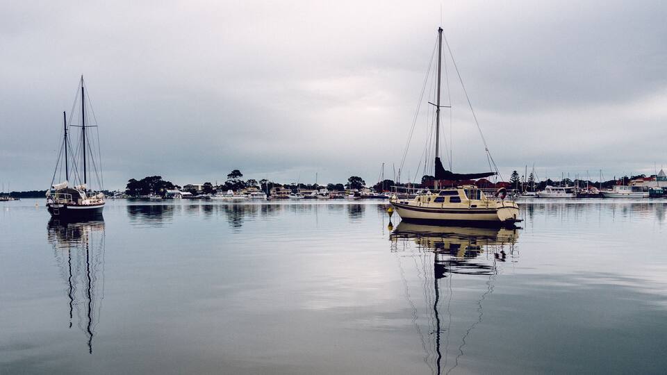 Calm waters with sailboats docked, a marina, and a town in the background.