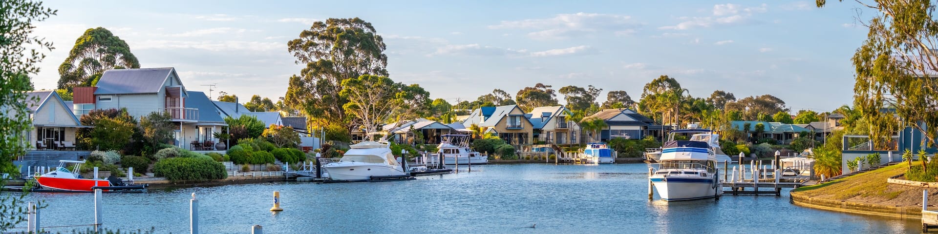panoramic view of a peaceful waterfront suburb featuring moored boats, modern homes. Australian waterside living, with private jetties, vessels, and well-maintained property. Paynesville, Australia