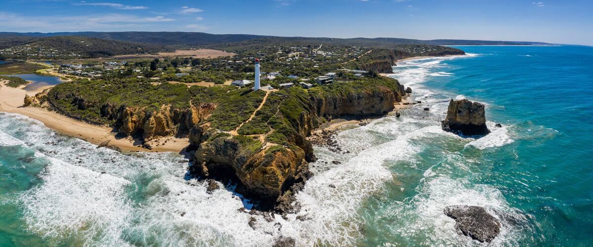 An aerial view of a coastal town with a lighthouse, beach, and surrounding cliffs.