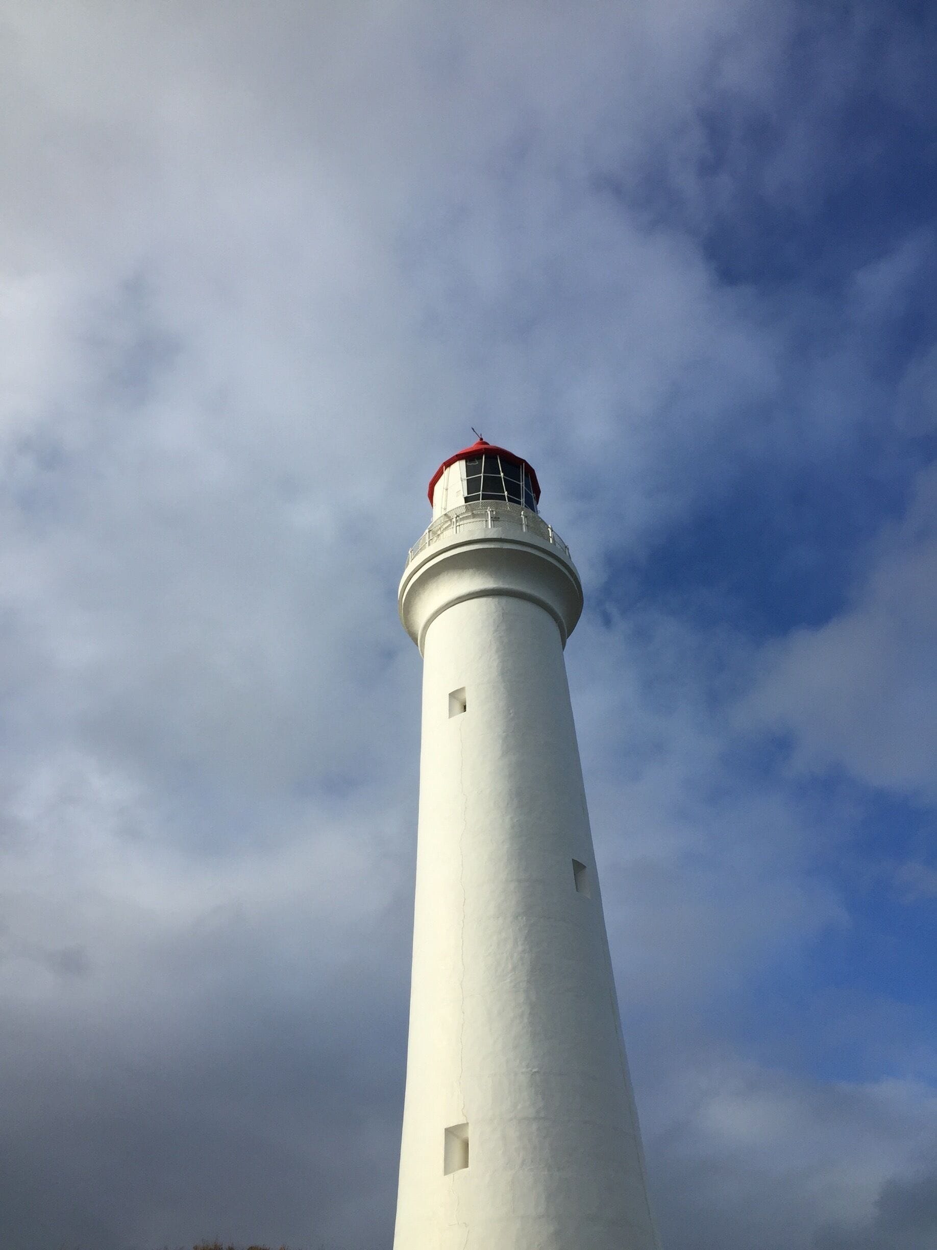 A tall white lighthouse with a red top against a cloudy sky.