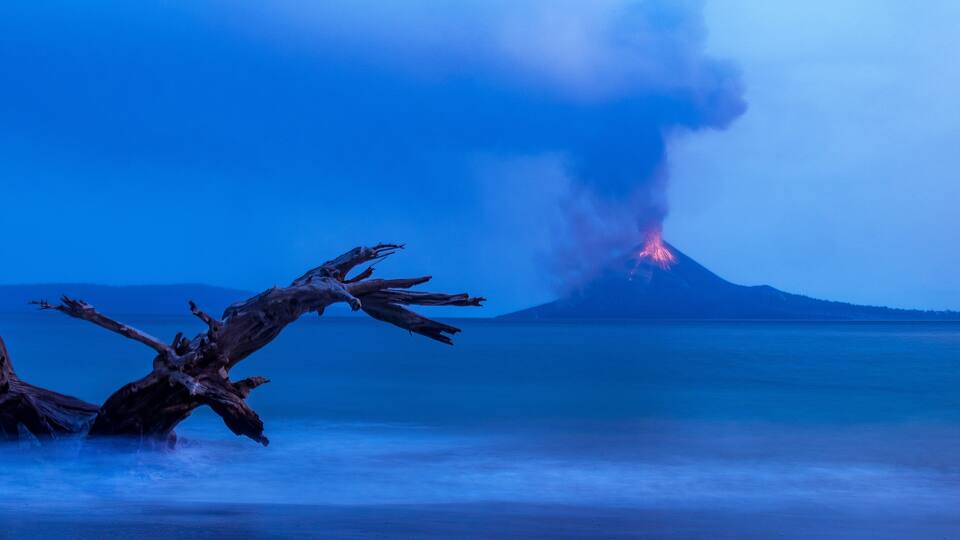 A volcanic eruption at night with smoke and lava visible.