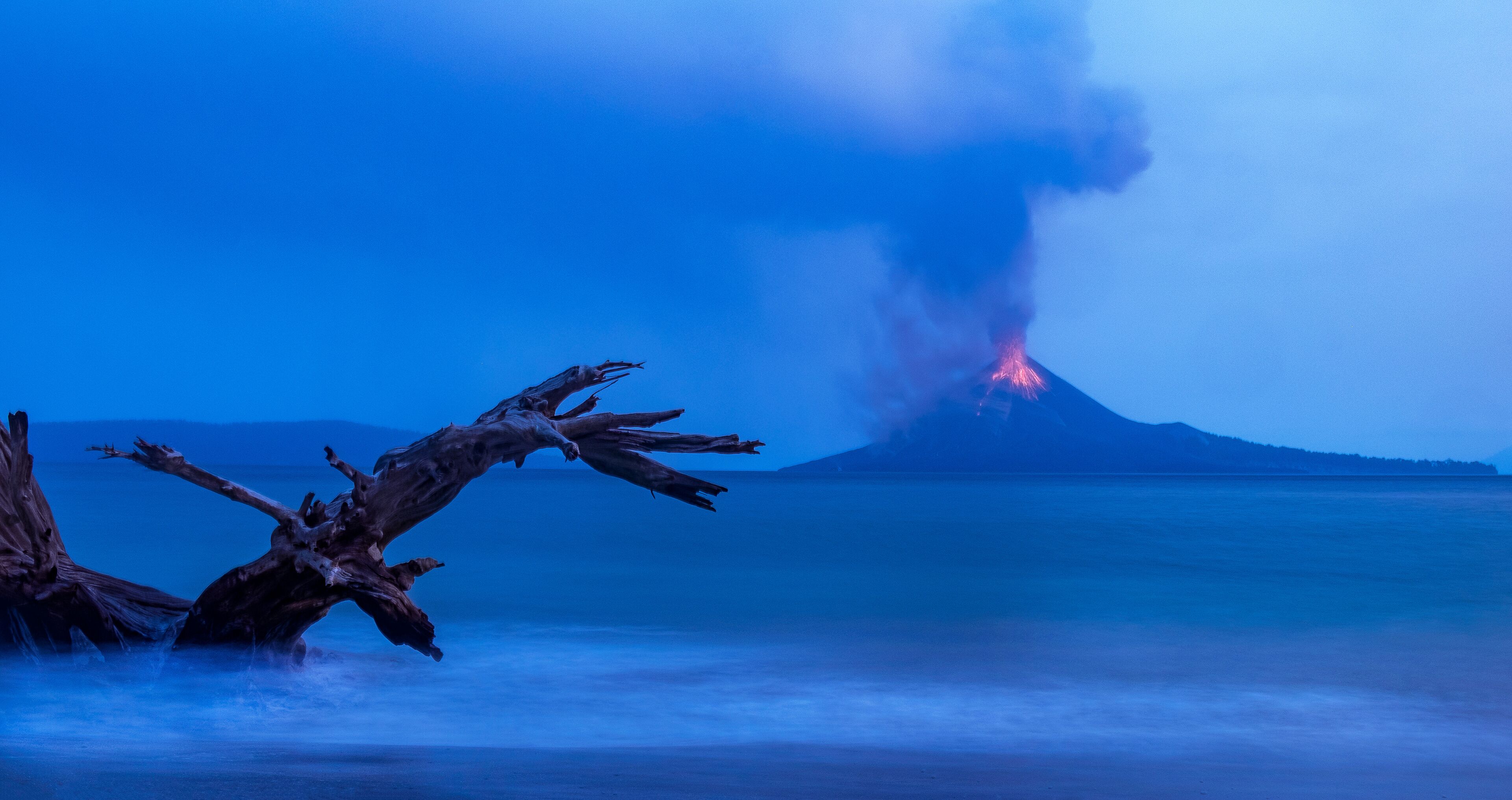 A volcanic eruption at night with smoke and lava visible.