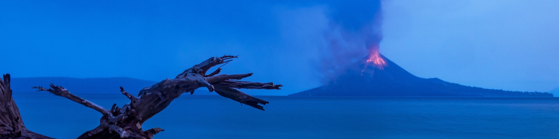 A volcanic eruption at night with smoke and lava visible.
