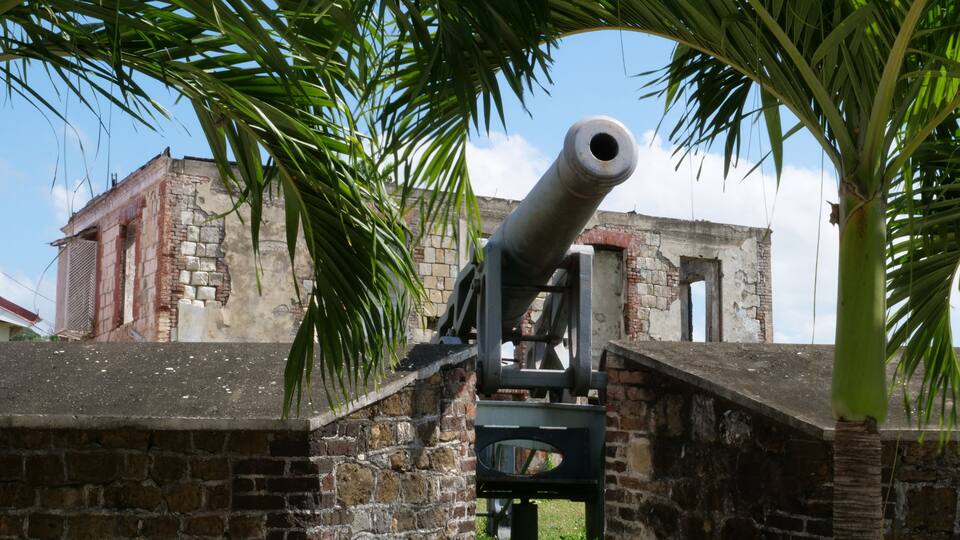 A cannon in a stone fortification with a brick building in the background.