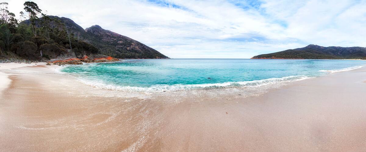 A beach with clear turquoise water, sandy shore, and mountains in the background.
