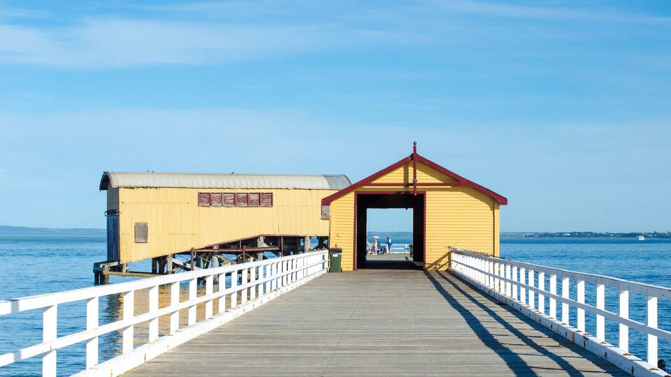 A wooden pier leading to a yellow and red pierhead structure with a white railing.