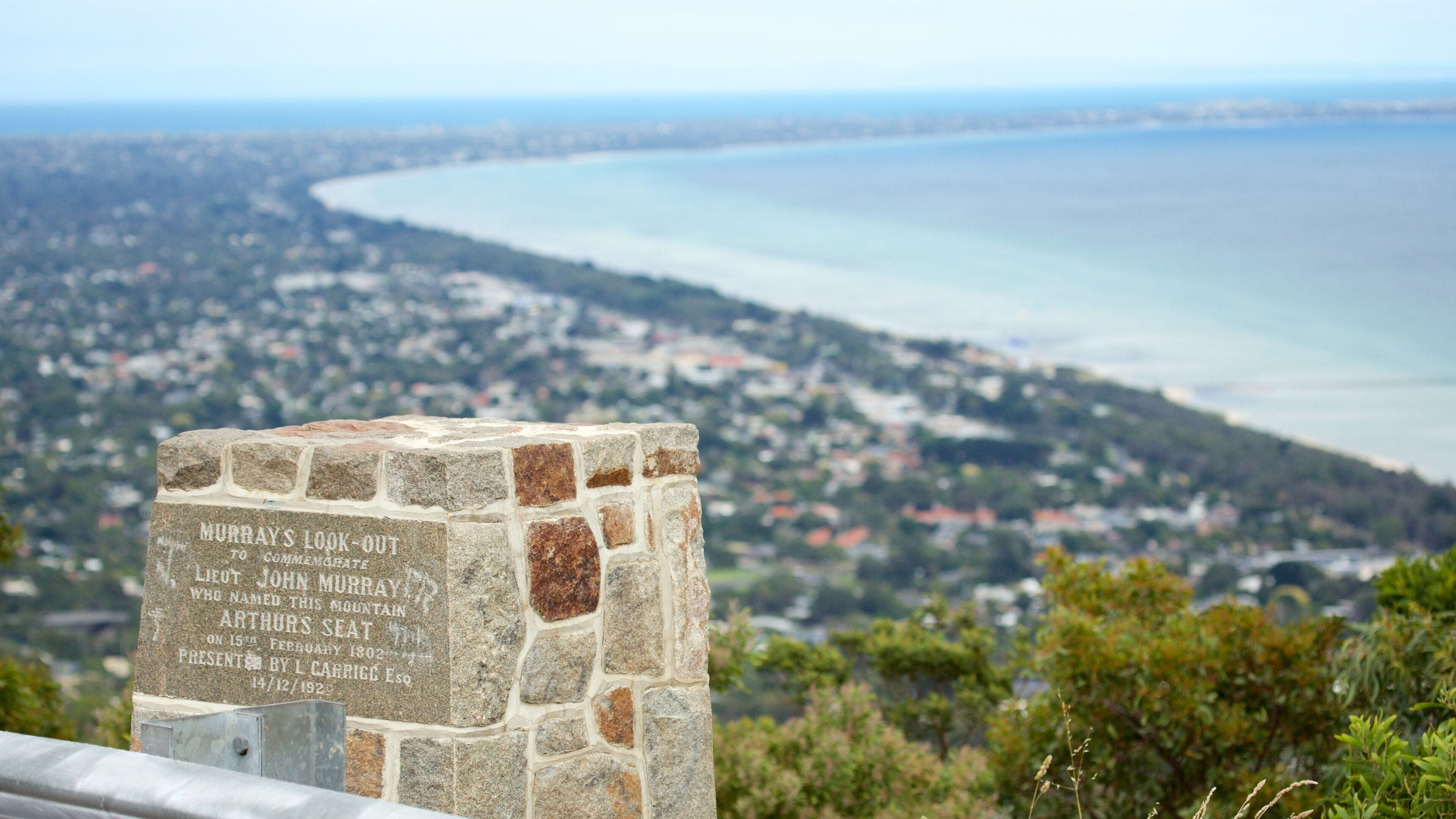 Un monumento de piedra con inscripciones, con vistas a un pueblo costero y una bahía.