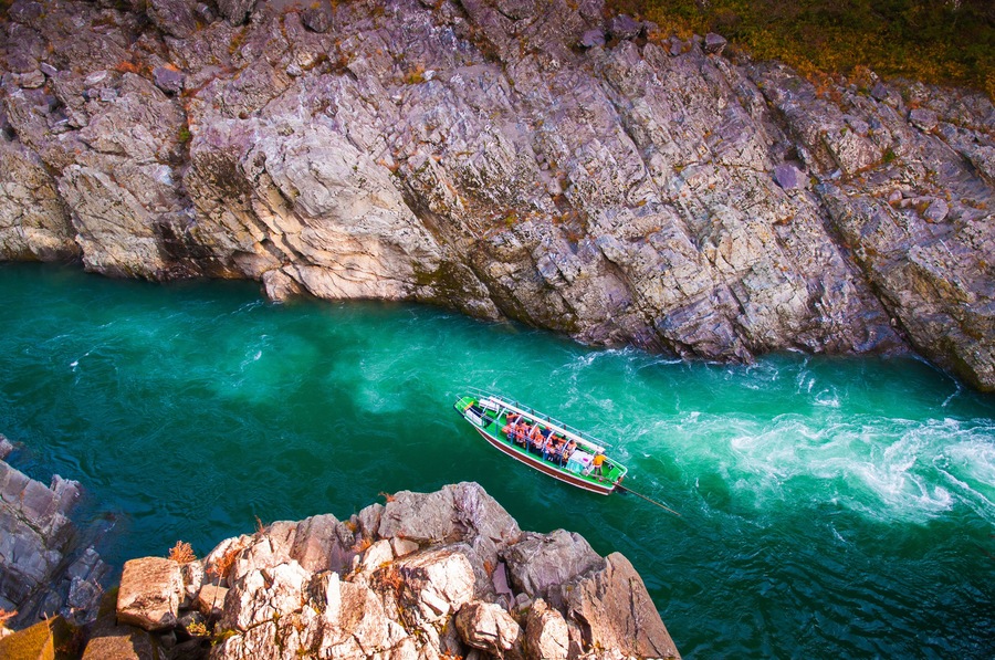 Una embarcación navega por un cañón estrecho y rocoso con agua turquesa cristalina.