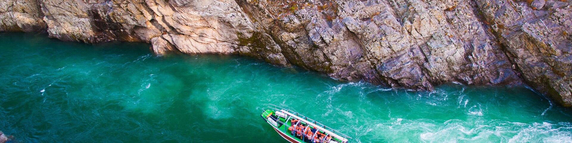 Una embarcación navega por un cañón estrecho y rocoso con agua turquesa cristalina.
