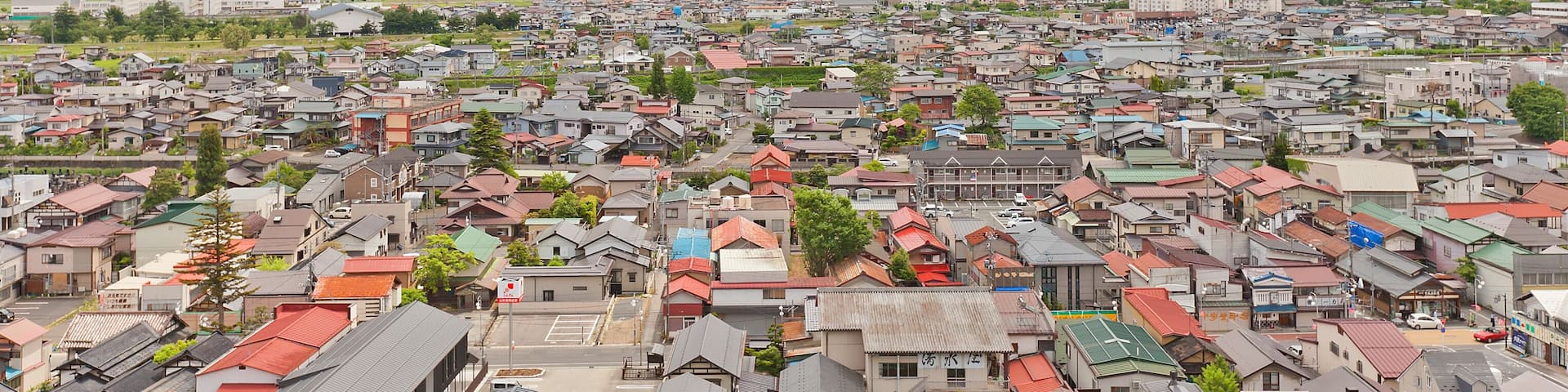 A town with red-roofed houses and green mountains in the background.