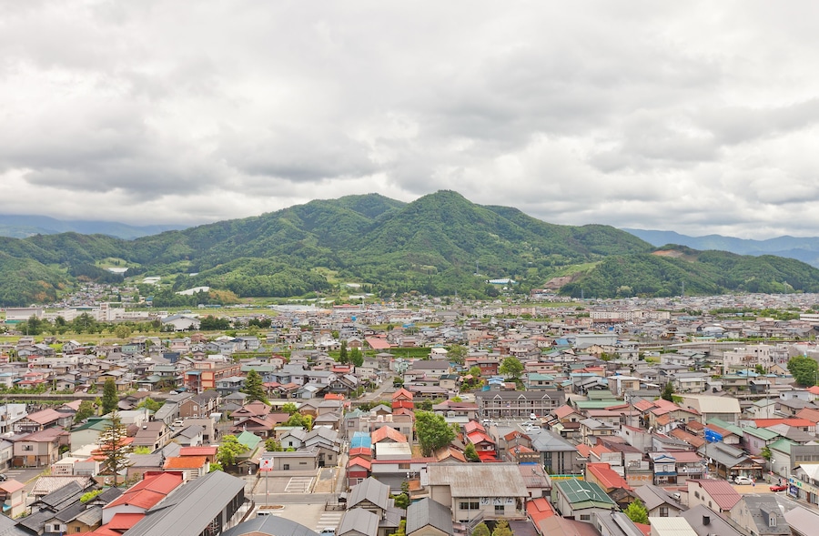A town with red-roofed houses and green mountains in the background.