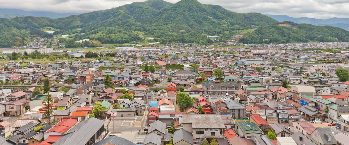 A town with red-roofed houses and green mountains in the background.
