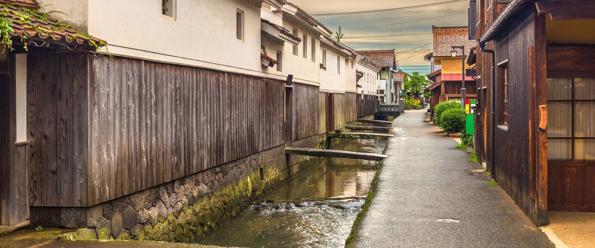 A narrow street with a water channel running alongside wooden buildings.